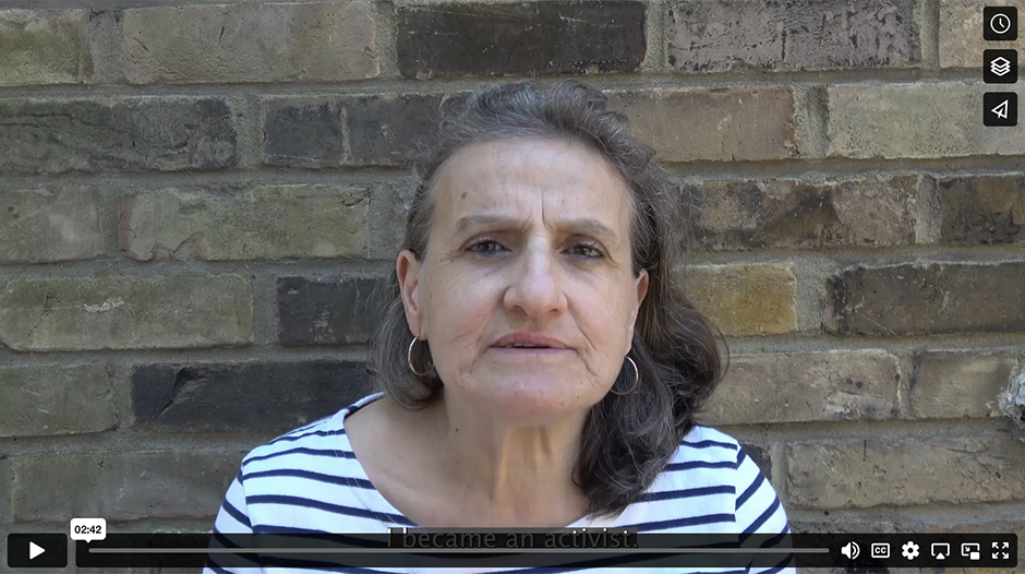 video still of Andria sitting in front of a yellowish brick wall